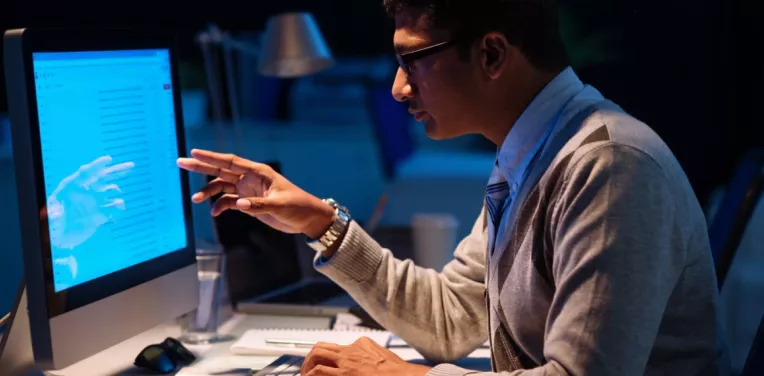 A man looking at a desktop computer screen and gesturing towards it